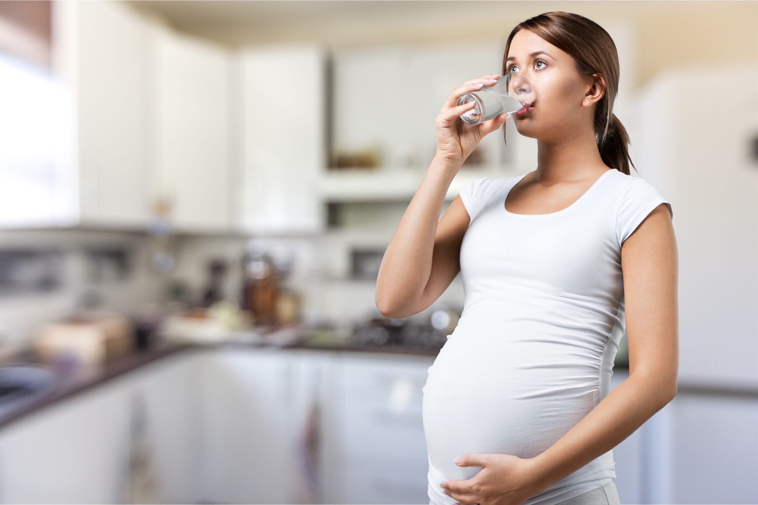 pregnant young woman white t shirt drinking water background scaled